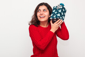 Young smiling woman wearing a red sweater holds a Christmas present in her hands. Happy female with a New Year gift box stands on the with background isolated. Winter holidays concept.