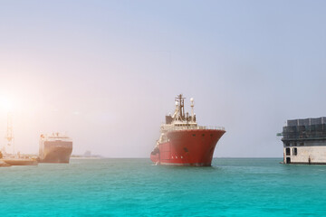 Tug boat sailing in the sea on port Tugboat making maneuvers, offshore supply boat in a calm weather day near floating dock of shipyard on harbor background.