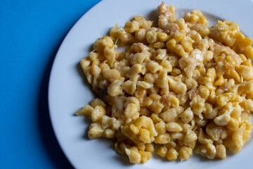 Close-up of a plate of German Käsespätzle (cheese Spaetzle) with onions on a plain blue background
