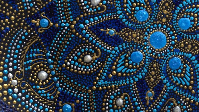 Decorative ceramic plate with black, blue and golden colors, painted plate rotating on background, closeup, top view. Decorative porcelain plate painted with acrylic paints, handwork, dot painting