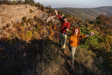 Young happy couple in love spending beautiful sunny autumn day in nature. Couple holding hands and climbing the hill.