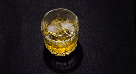 A glass of whiskey with ice on a black background. Copy the space.