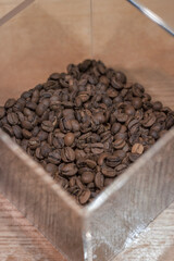 Perspective view on coffee beans in a plastic transparent box on a wooden table. Fresh medium roasted coffee beans.