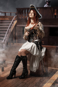 Young pirate female with long red hair. Woman is wearing a black corset bustier, tricorn hat , gun belt and armed with a pistol and sword.