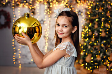 A big Golden Christmas ball in the hands of a girl. On the background of a garland of lights and a...