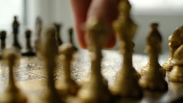 Close-up chess game. Metal chess pieces and the hand of a man who makes the first move with a pawn. The camera moves along the chessboard. UHD 4k video
