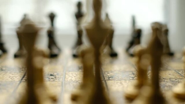 Close-up chess game. Metal chess pieces and the hand of a man who makes the first move with a pawn. The camera moves along the chessboard. UHD 4k video
