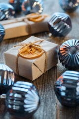 Lots of Christmas balls and presents packed in kraft paper on wooden background.