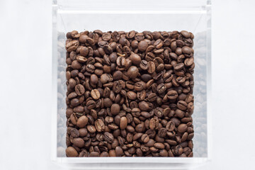 Top view of coffee beans in a transparent box on white background.