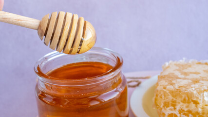 honey on a wooden stick from a full jar of honey with honeycombs on a plate