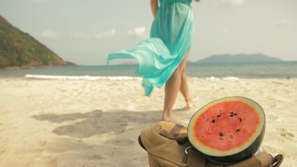 Naklejka na ściany i meble The cheerful woman in blur, against the background of a watermelon on tropical sand beach sea. Portrait attractive beautiful girl caucasian spend summer weekend in outdoor. White shirt beachwear.