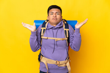 Young mountaineer man with a big backpack isolated on yellow background having doubts while raising hands