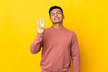 Young Ecuadorian man isolated on yellow background happy and counting three with fingers