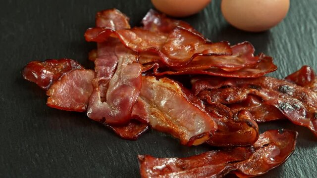 Super Slow Motion Shot of Roasted Bacon Slices Falling on Black Table at 1000 fps.