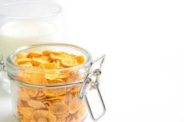 Corn flakes in a glass container and milk. White background. Copy space