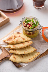 Healthy breakfast hummus with vegetables and peanuts in glass jar and flatbread on wooden board on the table