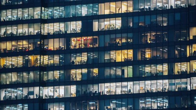 Silhouettes of office workers in the windows of modern building at evening time