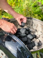 Fototapeta premium Man preparing grill in backyard with coal briquettes. Green garden in background.