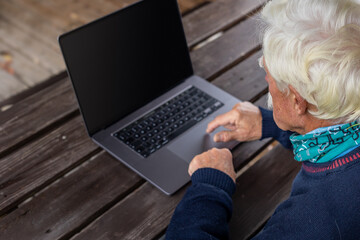 Old man working on laptop in his garden. A senior thoughtful man staring on the screen and making notes.