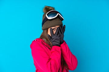 Teenager skier girl with snowboarding glasses over isolated blue background covering eyes and looking through fingers