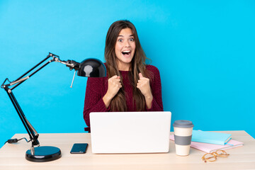 Teenager Brazilian girl with a laptop in a table celebrating a victory