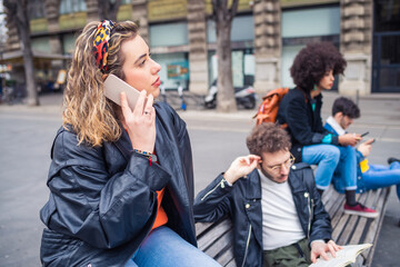 Four multiethnic people strangers or friends sitting bench outdoor using smartphone