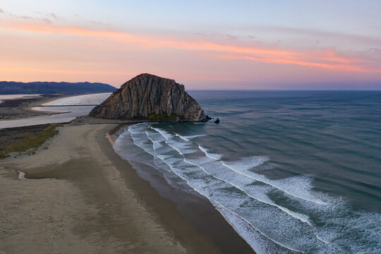 At dawn, the Pacific Ocean meets the iconic shoreline of Morro Bay, California. This coastal part of Central California is known for its beautiful and tranquil scenery.