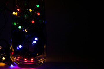 Colorful tangled christmas lights in glass on dark background with copy space.