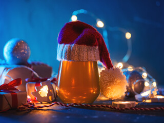 Christmas card for the festival, a glass of beer in a Santa hat on the festive table with gifts, garlands. Neon trend color background - obrazy, fototapety, plakaty