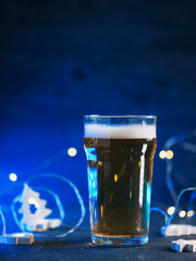 A glass of light beer on the table, a glowing blue background with a garland. Holiday festival