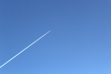 The plane flies high above the ground leaving a white trail. blue blue bright sky without clouds