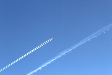 The plane flies high above the ground leaving a white trail. blue blue bright sky without clouds