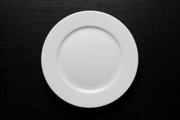 Round, white, empty plate on a black wooden background.