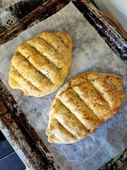  freshly baked white bread with herbs and garlic in the form of two loaves on a metal pan with baking paper