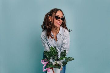 Nice beautiful woman with dark hair, wearing blue shirt, holding flowerpot and smiling, posing...