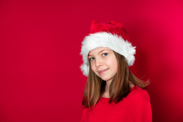 pretty young girl with Santa Claus cap and red pullover in front of red background