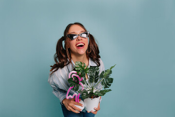 Portrait of amazed young woman with brunette wavy hair holding flowerpot and pink flamingo and looking at camera. studio shot, isolated background