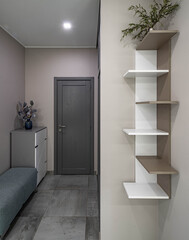 Entrance door in luxury apartment. Modern interior. Grey tile floor. Decorative flower. Empty shelves.