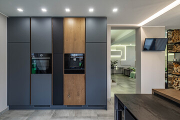 Contemporary interior of kitchen in luxury private house. Modern black kitchen set. Built-in oven....
