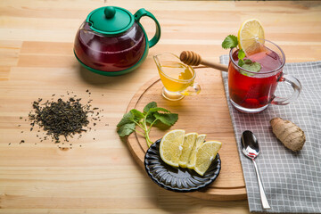 Berry tea in a cup next to lemon, honey, ginger lemon balm and a teapot on the table.