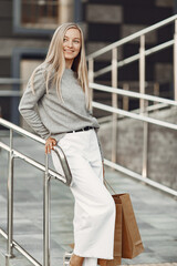 Woman in a summer city. Lady with brown bags. Woman in a gray sweater.