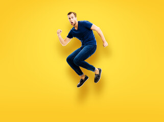 Fototapeta na wymiar Good unbelievable news, sales or holiday discounts concept - full body studio photo of jumping in air excited, shocked or surprised young man in blue casual clothing, isolated over yellow background.