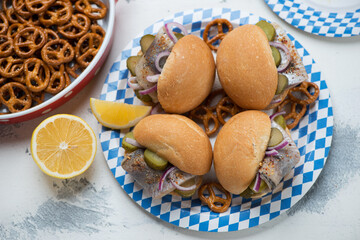 Blue and white carton plate with german fish sandwiches and mini pretzels over white concrete background, horizontal shot