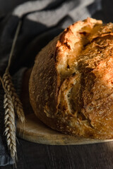 The handcrafted tartin bread lies on a wooden surface next to wheat ears. Farming and home baking concept
