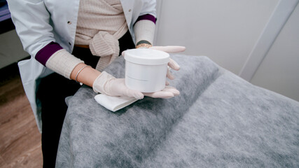 girl beautician in gloves holds face cream,
hands in gloves hold face cream