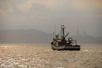 Old fishing boat navigating on the coast of the city of Santos in the late afternoon.
