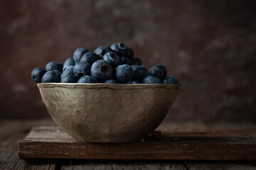 Bowl of fresh blueberries on rustic wooden table with copy space.