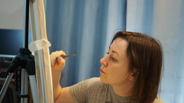 a young woman paints a picture on canvas with a brush.