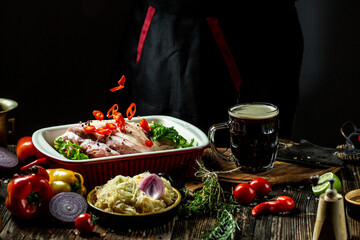 The chef prepares meat, Bavarian pork knuckle, throwing fresh meat with sweet peppers and beer on a black background, menu, recipe book, restaurants