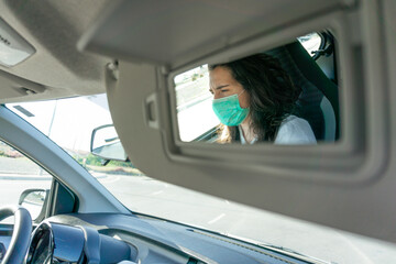A shot of a woman with protective face-mask focused through the passenger mirror of the car